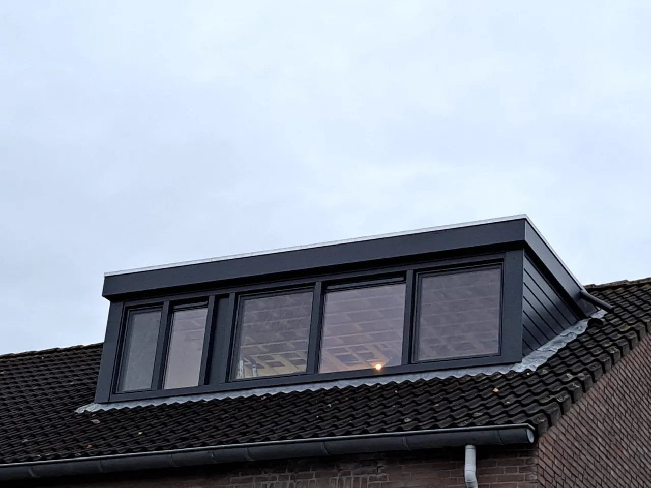 Brede antraciet dakkapel met vier ramen tegen een lichte lucht