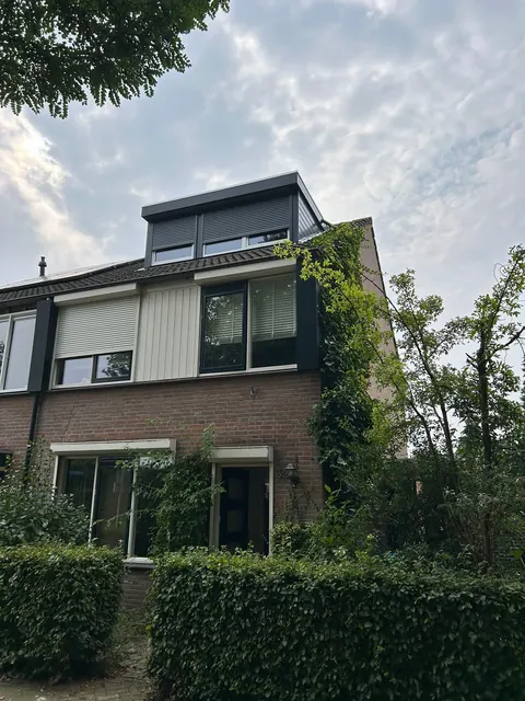 Donkere dakkapel op een hoekwoning met klimop